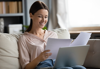 A Caucasian woman smiling while reading papers, seated on a couch.